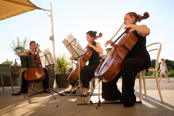 Drei Cellistinnen beim Spielen mit untergehender Sonne im Hintergrund.